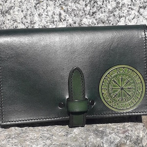 Peut inclure: Un portefeuille en cuir noir avec un motif de boussole vert et des runes. Le portefeuille a une fermeture à boucle.