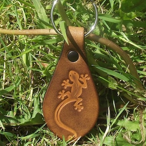 Peut inclure: Un porte-clés en cuir marron avec un anneau de clé en argent. Le porte-clés présente un motif en relief détaillé d'un lézard.