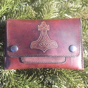 Puede incluir: Una cartera de cuero marrón con un diseño en relieve detallado de un martillo y un nudo celta. La cartera tiene dos broches de presión plateados.