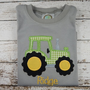 Puede incluir: Una camiseta gris con un dise&ntilde;o de tractor a cuadros verde y blanco y el nombre "Ridge" bordado en la parte inferior.