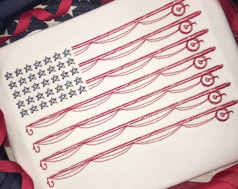 May include: White rectangular fabric with an embroidered American flag design. The flag's stars are black, and the stripes are represented by red fishing rods. Red and blue ribbons and a flag-themed fabric surround the main object.