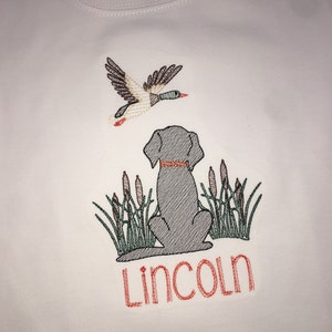 Peut inclure: Chemise blanche &agrave; manches longues avec un motif brod&eacute; repr&eacute;sentant un chien assis dans de hautes herbes avec un canard volant au-dessus. Le nom "Lincoln" est brod&eacute; sous le chien.