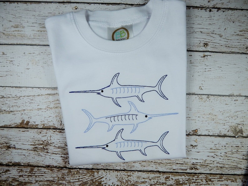 Pu&ograve; includere: Maglietta bianca con tre disegni di pesce spada blu ricamati.