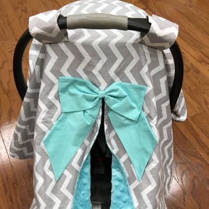 May include: Gray and white chevron car seat cover with a turquoise bow and matching plush lining.