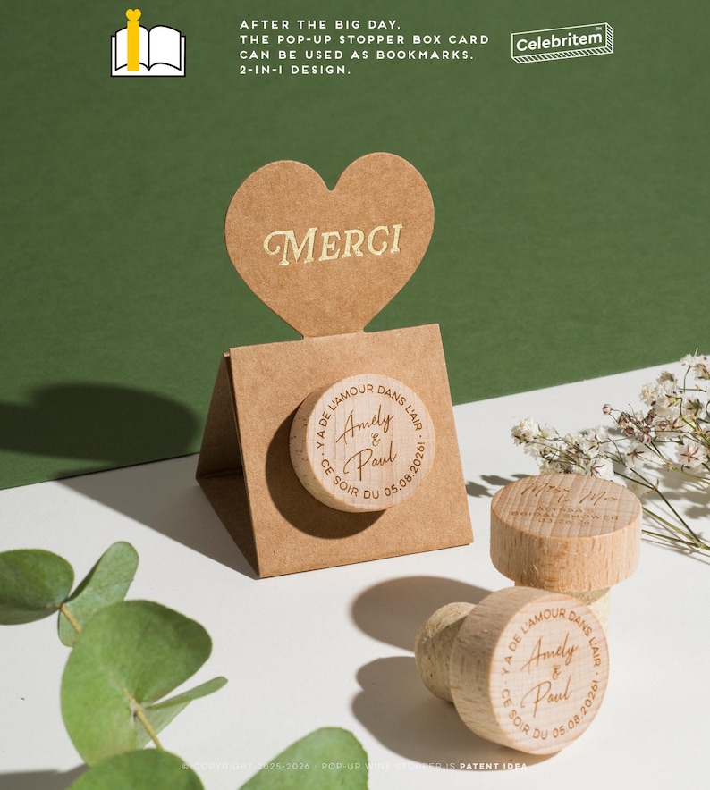 May include: A pop-up stopper box card with a heart-shaped topper that says "MERCI". The box features a wooden bottle stopper with the text "Amely & Paul" and the date "05.08.2026". The text "AFTER THE BIG DAY" is also visible.
