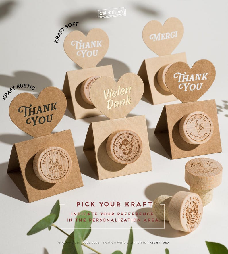 May include: A collection of heart-shaped kraft paper toppers with the words "Thank You" and "Merci" displayed above wooden wine stoppers. The stoppers are engraved with names, dates, and floral designs. The text "Pick Your Kraft" is also visible.