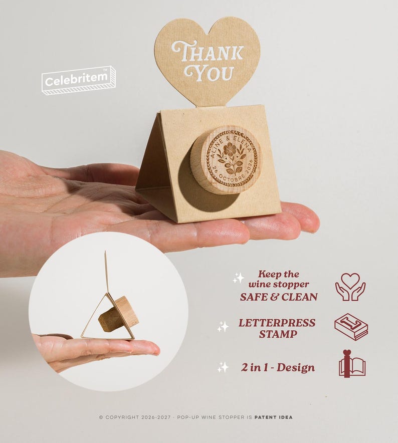 May include: A wooden wine stopper with a floral design and the names "Aline & Elena" and the date "26 October 2020" is displayed in a gift box with a heart-shaped "Thank You" tag. The stopper is held in a hand.
