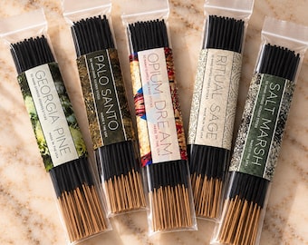 May include: Five clear plastic packages of black incense sticks, each with a paper label reading Georgia Pine, Palo Santo, Opium Dream, Ritual Sage, or Salt Marsh. Each package contains 50 hand-dipped incense sticks made in the USA.