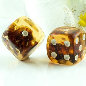 May include: Two amber dice with white dots, one on a white background and the other on a white flower.