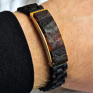 May include: A black silicone bracelet with a gold-toned rectangular plate featuring a brown and black patterned design.