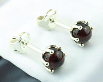 May include: A pair of silver stud earrings with a dark red gemstone in each. The gemstones are set in a silver crown-like design.