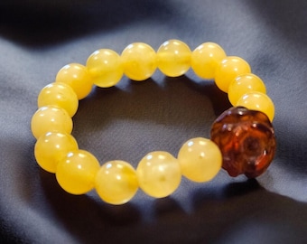 May include: A beaded bracelet featuring large, round, yellow beads. The bracelet includes a single, dark brown, intricately carved bead. The bracelet is displayed on a dark, textured surface.