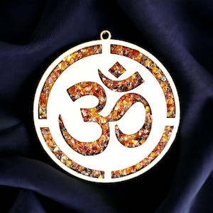 May include: A round, gold-coloured pendant with a white Om symbol cut out of the centre. The pendant is filled with small, amber-coloured stones.