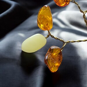 May include: A necklace made of amber and white stones, strung on a gold wire. The amber stones are a deep orange color and have a natural, irregular shape. The white stones are smooth and oval-shaped.