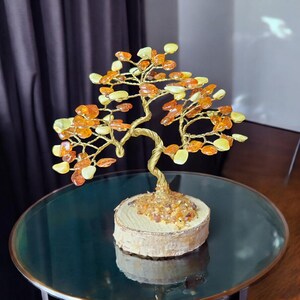 May include: A gold wire tree sculpture with amber stones for leaves. The tree is on a wooden base and is sitting on a glass table.