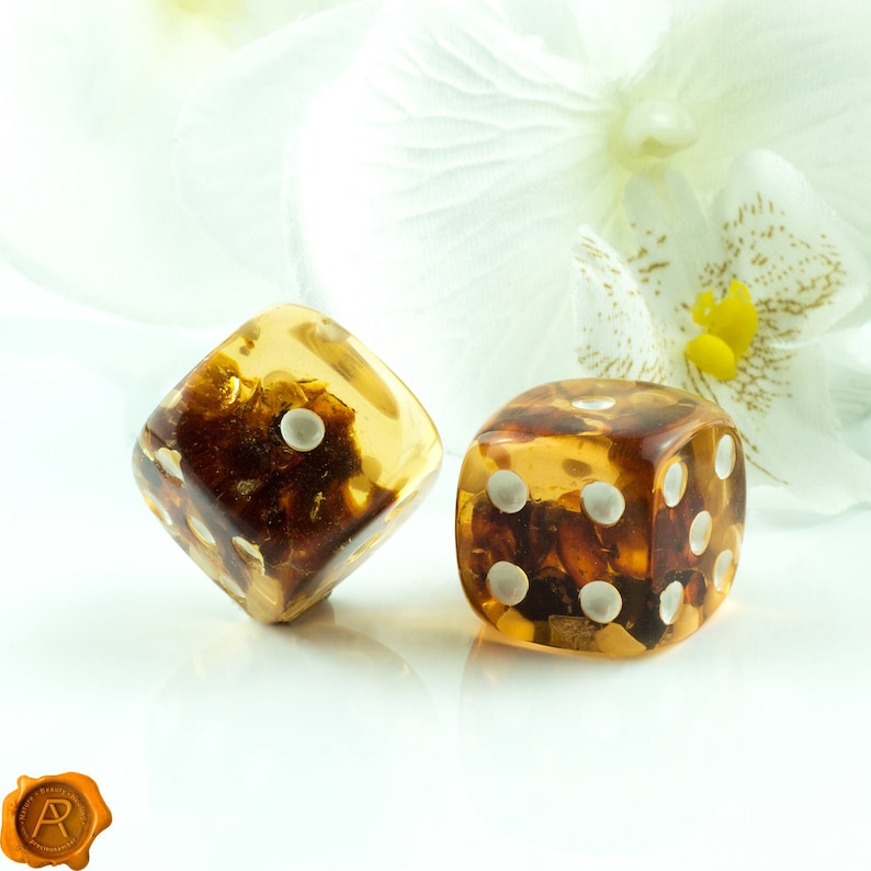 May include: Two amber dice with white dots, one on a white background and the other on a white flower.