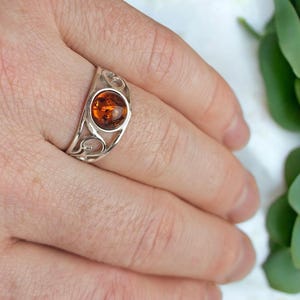 May include: A silver ring featuring a round amber stone set in a delicate, swirling design.
