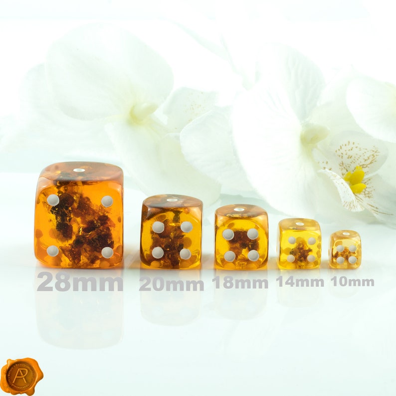 May include: Five amber dice of different sizes, ranging from 10mm to 28mm. The dice are translucent and have white dots on each side. The dice are arranged in a row from largest to smallest.
