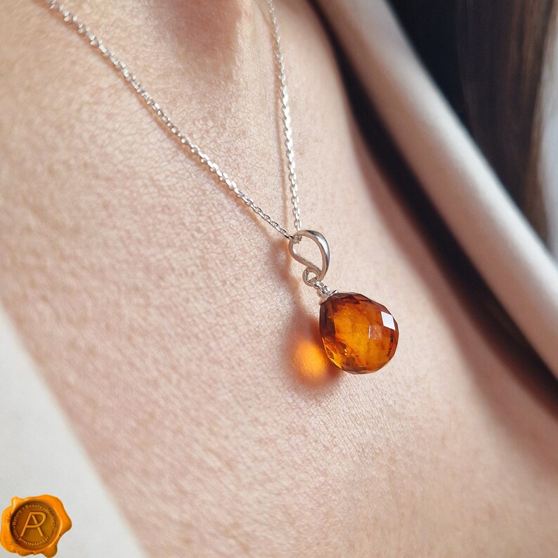 Pu&ograve; includere: Una collana con catena d'argento con un ciondolo in ambra a forma di lacrima.