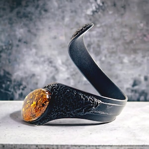 Pode incluir: Um bracelete de couro preto com um design intrincado e uma grande pedra de âmbar.