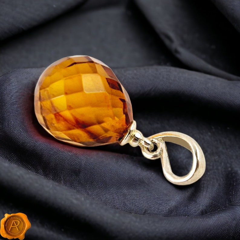 Pu&ograve; includere: Un ciondolo in oro con una pietra preziosa di ambra sfaccettata. L'ambra &egrave; di colore arancio intenso e ha una finitura liscia e lucida. Il ciondolo &egrave; attaccato a una catena d'oro.