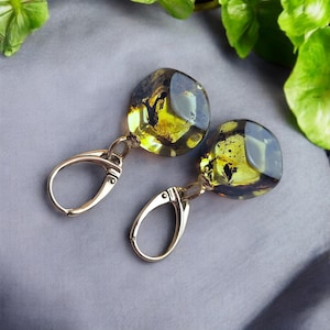 May include: A pair of gold hoop earrings with amber stones. The amber stones are a dark green color with yellow and black inclusions.