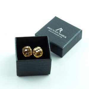 May include: Two amber dice with white dots in a black gift box. The box has the text "Precious Amber" and a website address printed on the top.