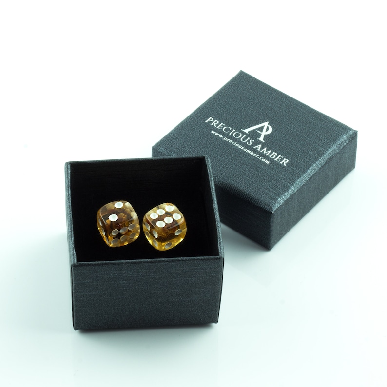 May include: Two amber dice with white dots in a black gift box. The box has the text "Precious Amber" and a website address printed on the top.