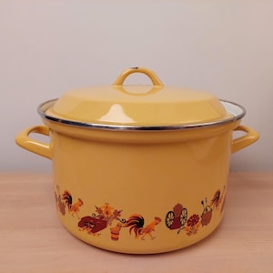 Può includere: Pentola in smalto giallo con coperchio. La pentola presenta una fascia decorativa con galli e motivi floreali attorno alla base. Il coperchio ha una maniglia ad anello. La pentola ha due manici laterali e un bordo argentato.
