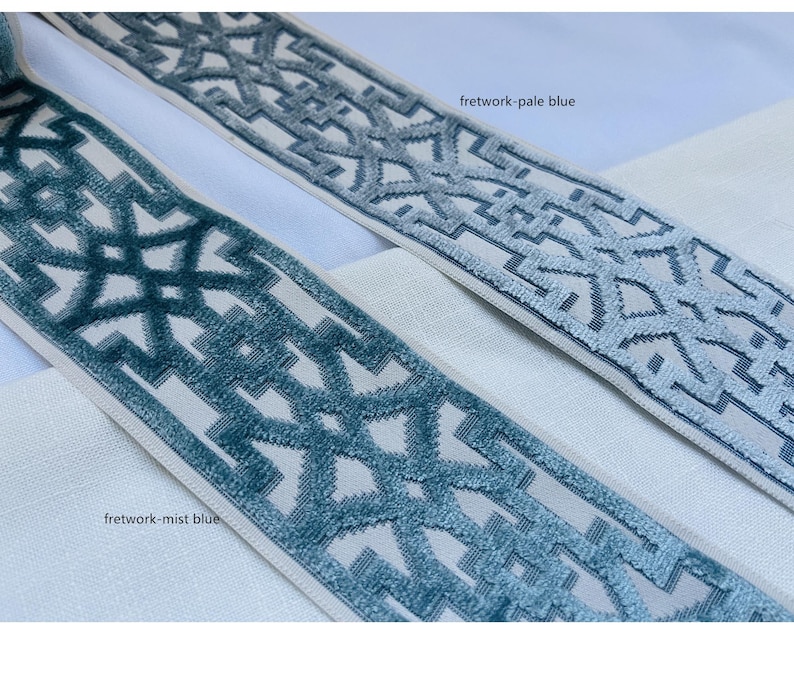 May include: Two samples of trim fabric with a geometric pattern. The trim on the top is a pale blue color and the trim on the bottom is a darker blue color. The text "fretwork-pale blue" is written above the top trim and the text "fretwork-mist blue" is written below the bottom trim.
