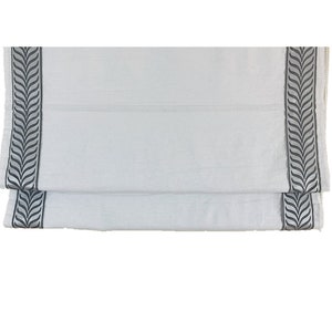 May include: White roman shade with a black leaf pattern border.