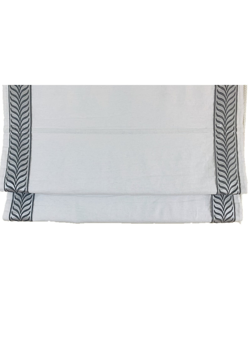 May include: White roman shade with a black leaf pattern border.