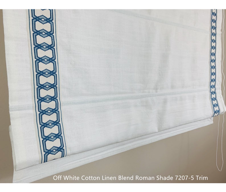 May include: Off white cotton linen blend Roman shade with a blue geometric pattern trim. The shade is partially rolled up, showing the fabric texture. The text "Off White Cotton Linen Blend Roman Shade 7207-5 Trim" is visible at the bottom of the image.