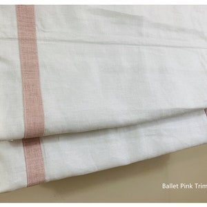 May include: White roman shade with a pink trim. The trim is a woven fabric with a subtle texture. The shade is folded in half, showing the trim on both sides. The text "Ballet Pink Trim" is visible at the bottom of the image.