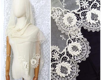 May include: A white lace shawl with a delicate floral pattern. The shawl is made of a sheer fabric and has a scalloped edge.