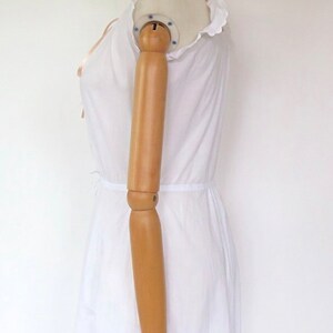 Op de afbeelding: Witte katoenen jurk met een gerimpelde halslijn en een gerimpelde zoom. De jurk is op een wit mannequin.