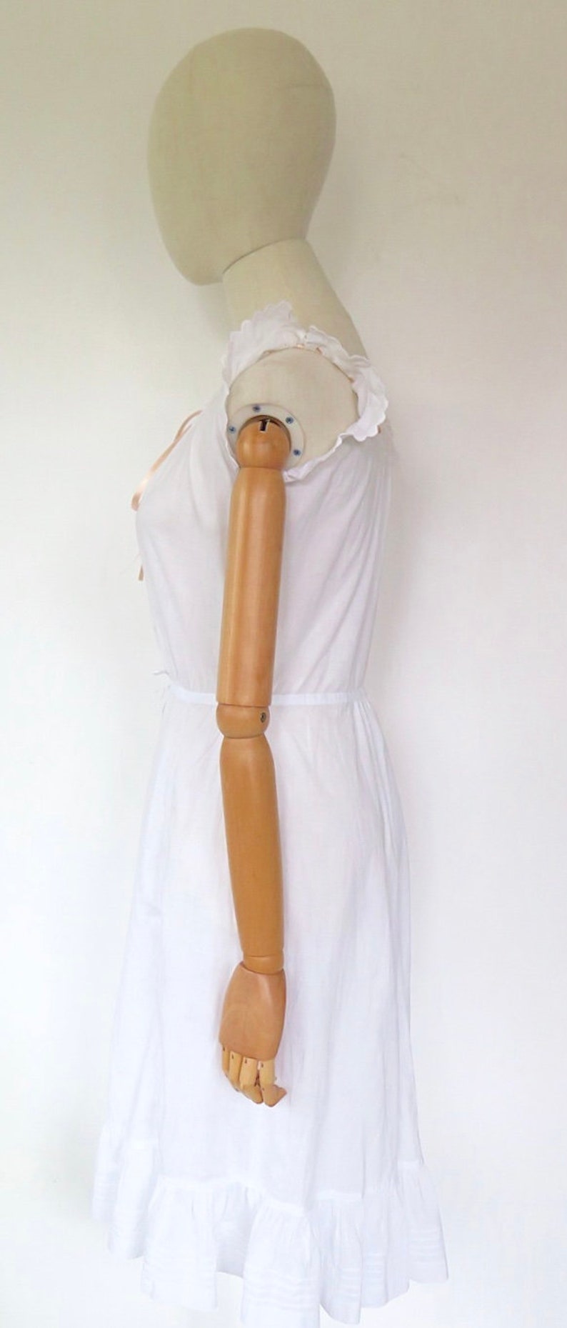 Op de afbeelding: Witte katoenen jurk met een gerimpelde halslijn en een gerimpelde zoom. De jurk is op een wit mannequin.