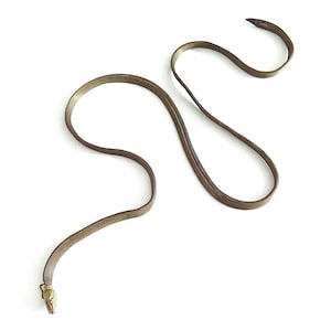 Könnte beinhalten: Eine bronzefarbene, schlangenförmige Halskette mit detailliertem Schlangenkopf. Die Halskette besteht aus einem netzartigen Material und liegt auf weißem Hintergrund. Der Körper der Schlange ist gewunden.