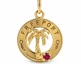 Könnte beinhalten: Ein goldener runder Anhänger mit der Gravur FREEPORT am oberen Rand. In der Mitte befindet sich die Silhouette einer strukturierten Palme mit einem kleinen, runden, leuchtend roten Edelstein am Fuß des Baumstamms.
