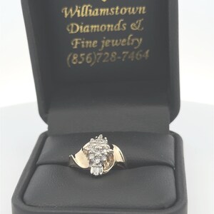 May include: A gold ring with a cluster of small diamonds set in a twisted band. The ring is in a black velvet ring box with the text "Williamstown Diamonds & Fine Jewelry (856)728-7464" printed on the inside.