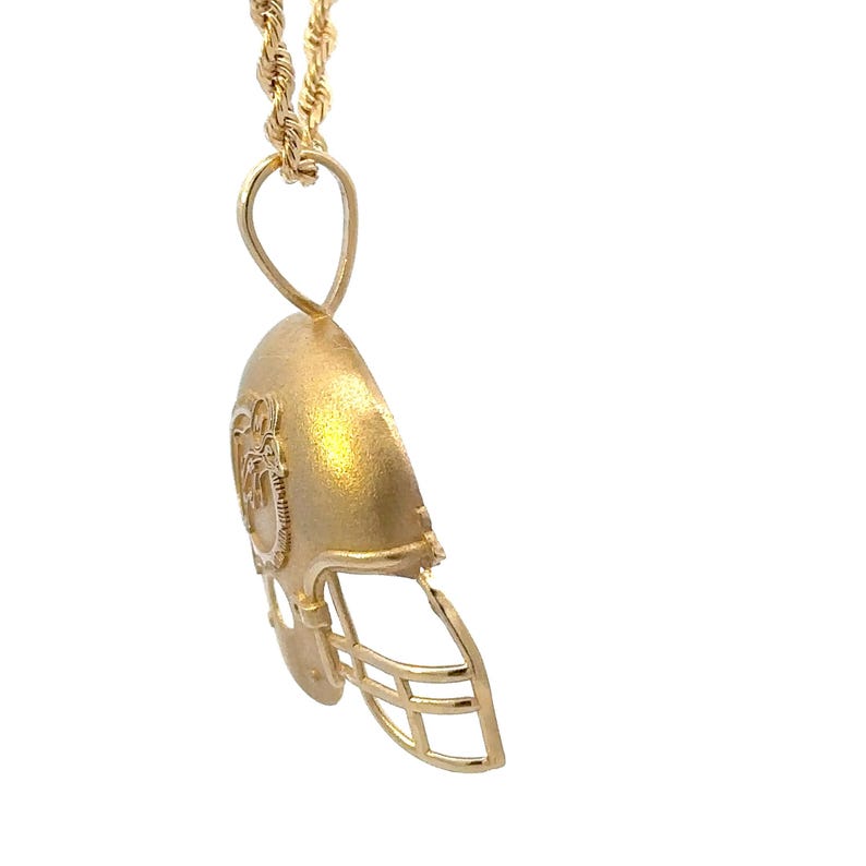 K&ouml;nnte beinhalten: Ein goldfarbener Anh&auml;nger in Form eines Footballhelms mit strukturierter Oberfl&auml;che und einem seitlichen Widder-Logo. Der Helm h&auml;ngt an einer goldfarbenen Kordelkette mit einer runden &Ouml;se und zeigt ein detailliertes Gitter sowie eine Helmschale.