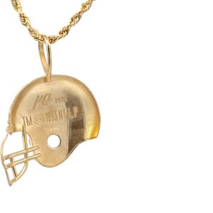 K&ouml;nnte beinhalten: Ein goldfarbener Footballhelm-Anh&auml;nger an einer passenden gedrehten Kordelkette. Der Helm verf&uuml;gt &uuml;ber einen Gesichtsschutz und ist an der Seite mit dem Text "MK 14K TM &copy; 1993 NFLP" graviert. Der Anh&auml;nger hat eine polierte Oberfl&auml;che und eine &Ouml;se.