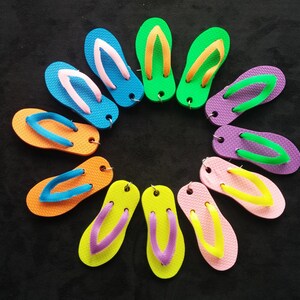 May include: A collection of ten colourful flip-flops arranged in a circle on a black background. The flip-flops are made of rubber and have a variety of colours, including blue, green, orange, pink, and yellow.