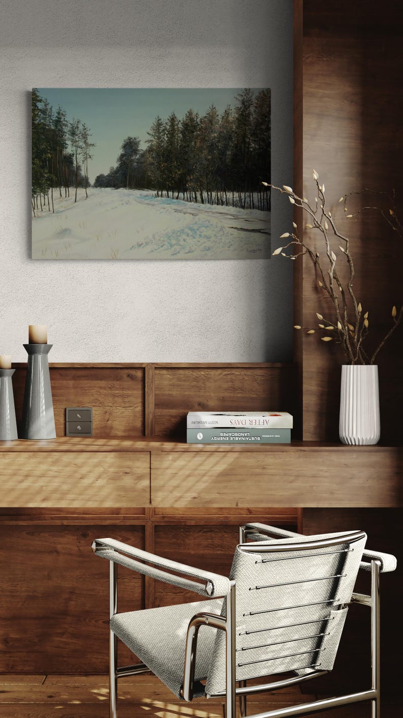 May include: An oil painting depicts a snowy forest scene with a path leading into the distance. The artwork hangs above a wooden cabinet with books and decorative items. A modern chair with a metal frame and gray fabric sits in front.