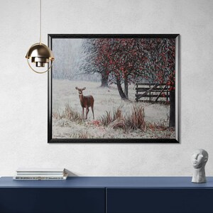 Pu&ograve; includere: Un dipinto paesaggistico incorniciato raffigura un cervo in un campo innevato. Alberi con foglie rosse e una staccionata in legno sullo sfondo. L'opera &egrave; esposta su un mobile blu, con una lampada a sospensione dorata sopra.