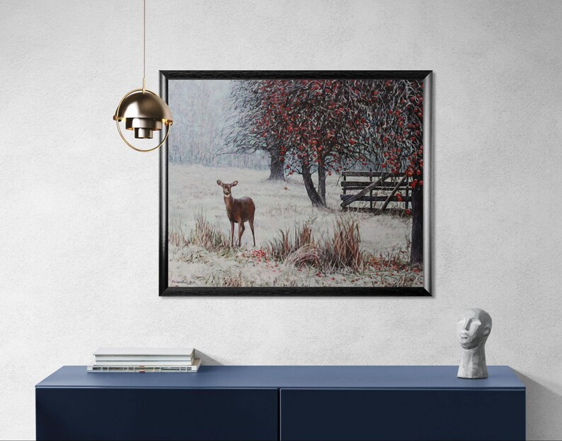 Pu&ograve; includere: Un dipinto paesaggistico incorniciato raffigura un cervo in un campo innevato. Alberi con foglie rosse e una staccionata in legno sullo sfondo. L'opera &egrave; esposta su un mobile blu, con una lampada a sospensione dorata sopra.
