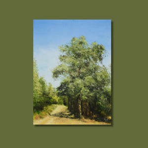 May include: Oil painting of a sunlit dirt path winding through a forest. The artwork features a large tree with lush green foliage on the right, a bright blue sky, and other trees in the background. The painting is framed.