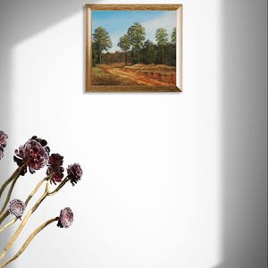 Pu&ograve; includere: Un dipinto di paesaggio incorniciato raffigura un sentiero attraverso una foresta con alberi e cielo blu. L'opera d'arte ha una cornice color oro ed &egrave; esposta su una parete bianca. I colori del dipinto includono verde, marrone e blu.