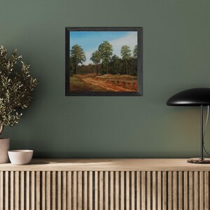 Pu&ograve; includere: Un dipinto di paesaggio incorniciato raffigura un sentiero sterrato che si snoda attraverso una foresta di alberi verdi sotto un cielo blu. Il dipinto &egrave; in una cornice nera ed &egrave; appeso a una parete verde. Una piccola pianta in vaso e una lampada sono in primo piano.