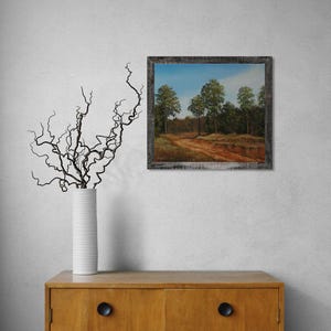 Pu&ograve; includere: Un dipinto di paesaggio incorniciato raffigura uno stradone che conduce in una foresta con alberi verdi sotto un cielo blu. Il dipinto ha una cornice in legno rustica e usurata. Un vaso bianco con rami scuri &egrave; su un mobile di legno.